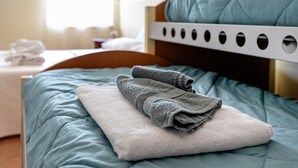 A neatly made bed with a teal comforter, a white pillow, and folded towels.