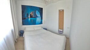A bedroom with a bed, a painting of a cave, a small table, and a wooden door. - Vacaciones 'La Orilla' with Private Terrace, Balcony, and Wi-Fi (Costa Calma)
