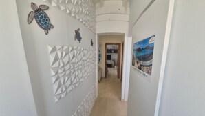 A hallway with a geometric wall design, a poster of a coastal scene, and a turtle decoration. - Vacaciones 'La Orilla' with Private Terrace, Balcony, and Wi-Fi (Costa Calma)