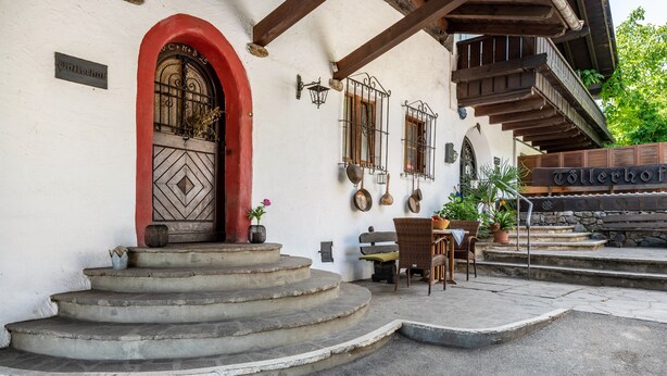 A building with a red arched entrance, a set of outdoor steps, and a wooden balcony.