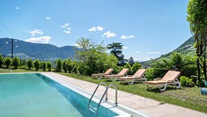 A swimming pool with a clear view of mountains in the background, surrounded by lounge chairs and greenery.