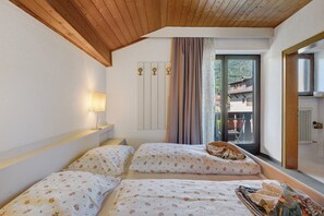 Een slaapkamer met twee bedden, een raam met gordijnen, een lamp en uitzicht op een balkon.