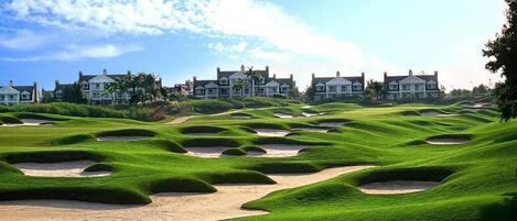 A golf course with bunkers and a clubhouse in the background.