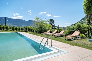 A swimming pool with clear water, surrounded by lounge chairs and a view of mountains.