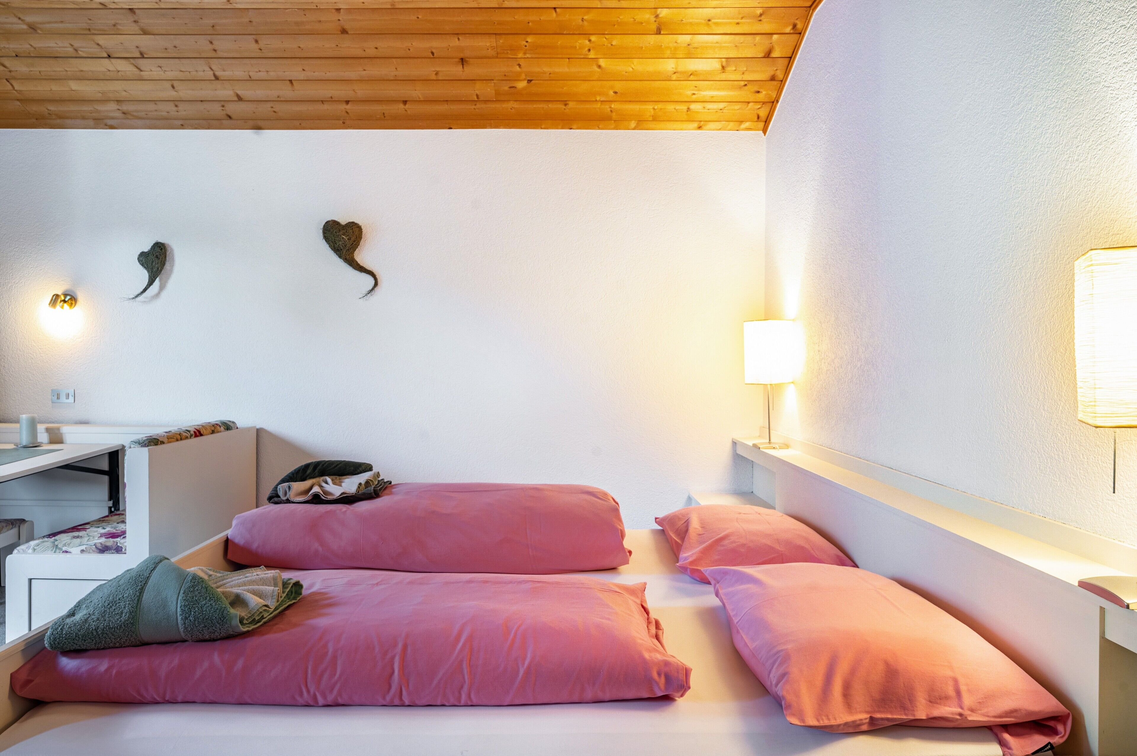 A room with two beds, a desk, and a wall-mounted light.