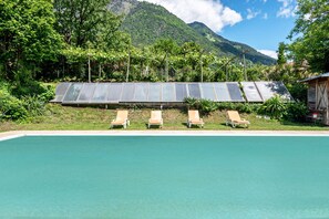 A pool with four sun loungers and solar panels in a lush, mountainous setting. - Apartment 'Weinberg 2' with Mountain View, Shared Pool and Wi-Fi (Algund)