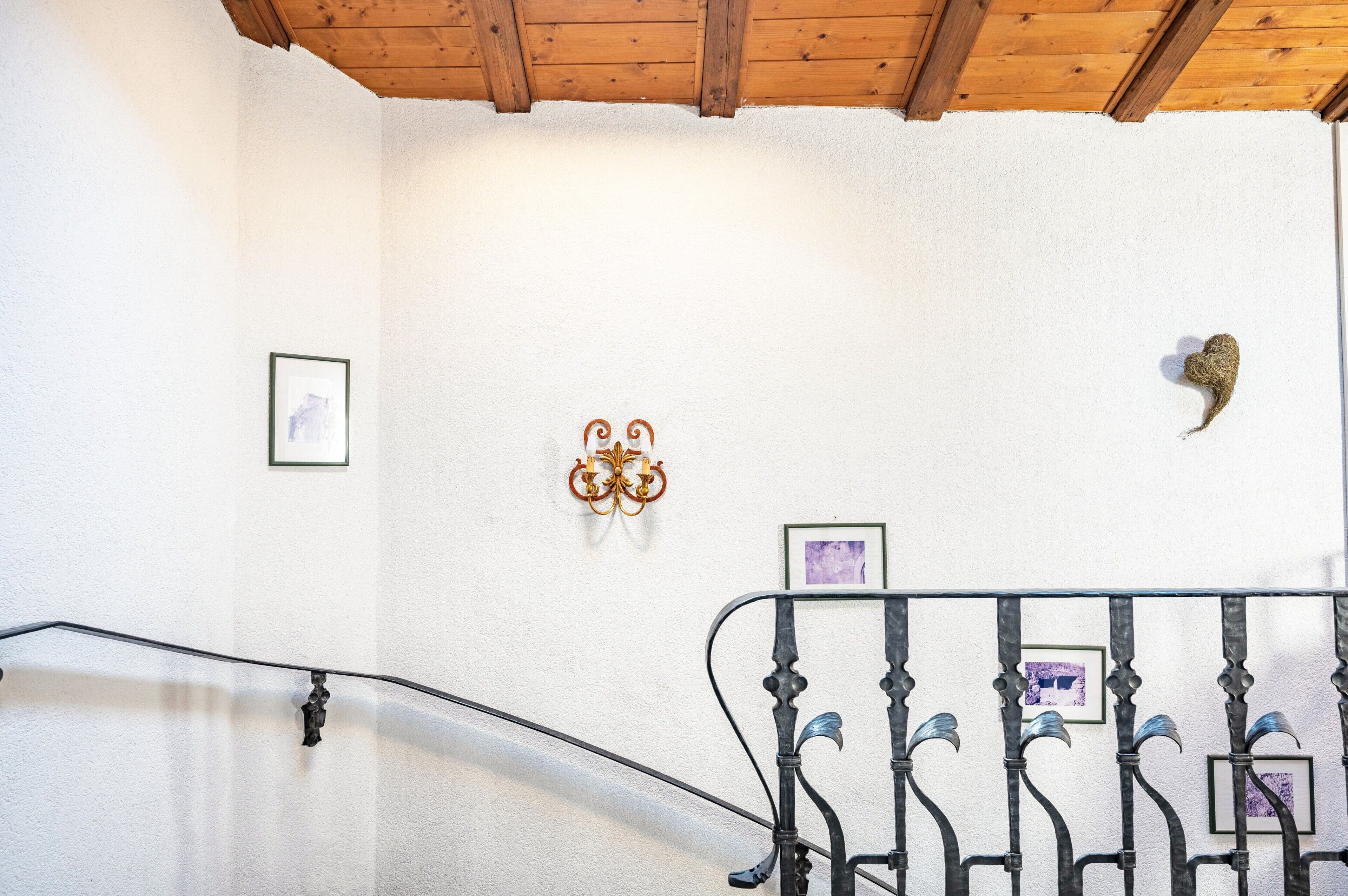 A staircase with a metal railing, a wooden ceiling, and wall-mounted artwork.