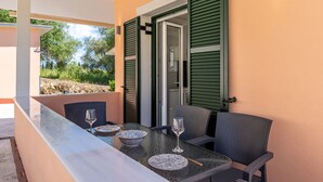 An outdoor dining area with a table, chairs, and a glass door leading to a garden. - Luxury Stay Apartment with Mountain View, Wi-Fi, and Air Conditioning (Kerkira)