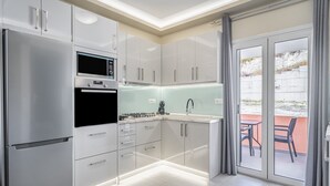 A modern kitchen with a refrigerator, oven, microwave, and a sliding glass door leading to an outdoor area. - Luxury Stay Apartment with Mountain View, Wi-Fi, and Air Conditioning (Kerkira)
