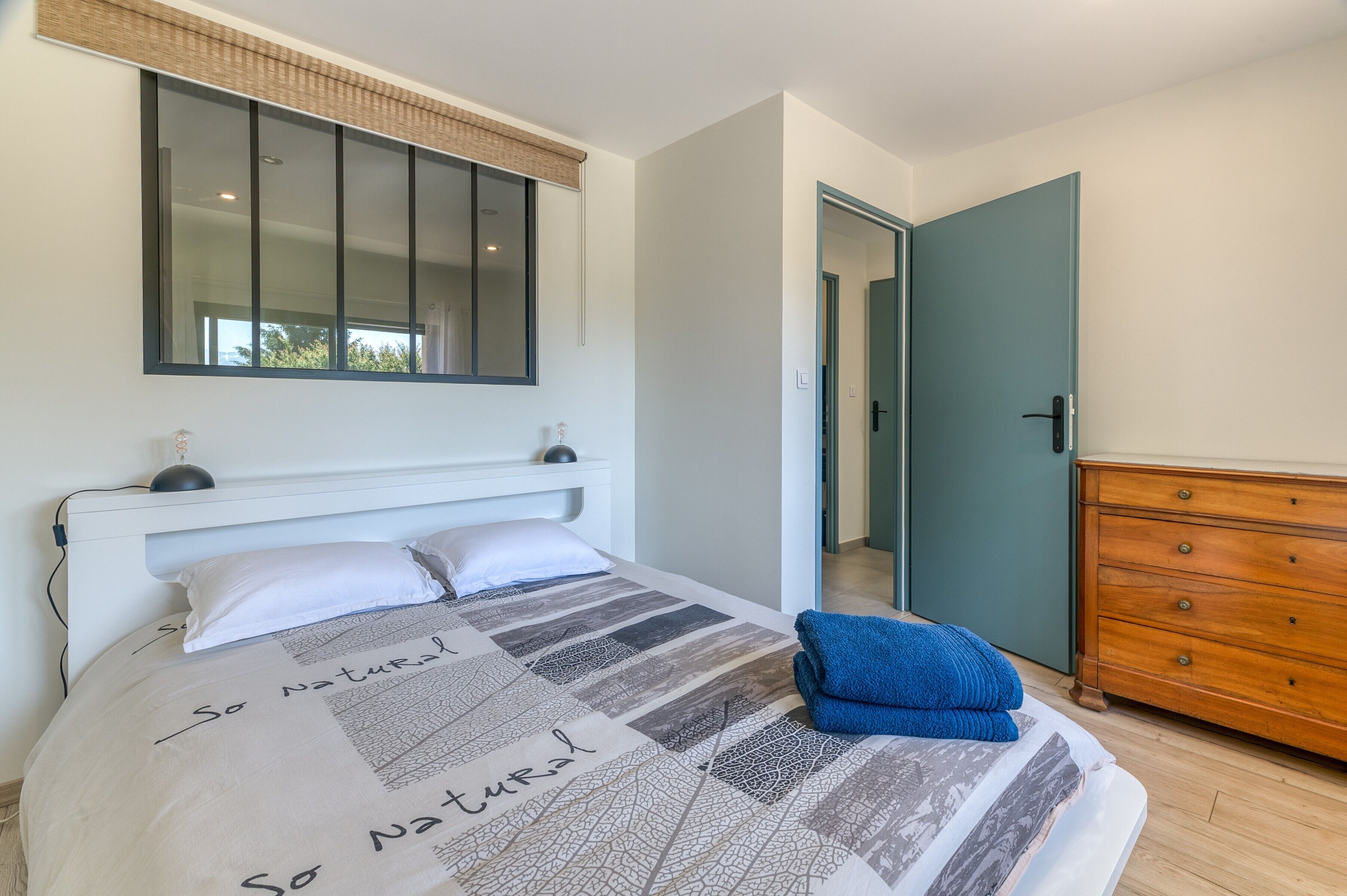 A bedroom with a bed, a dresser, a mirror, and a door leading to another room.