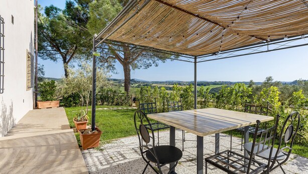 Un patio al aire libre con mesa y sillas, una pérgola y vistas al campo.