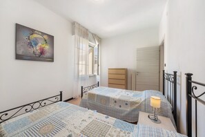 Une chambre avec deux lits, une fenêtre avec des rideaux, une commode et un tableau au mur.