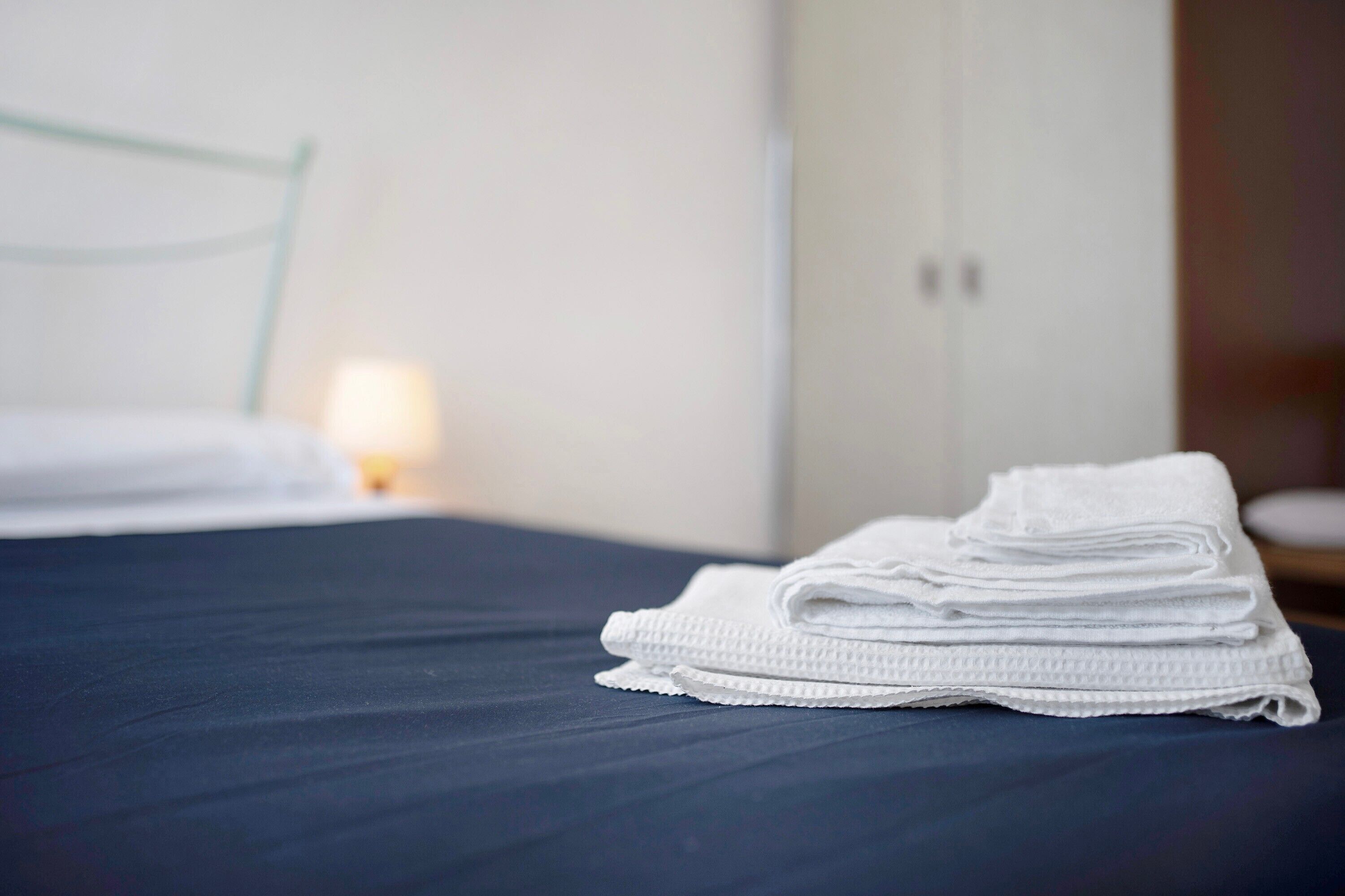 Una cama bien hecha con una colcha azul oscuro y una pila de toallas blancas a un lado.