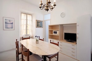 A dining area with a marble table, wooden chairs, a chandelier, a television on a cabinet, and artwork on the walls. - Apartment 'Edda' with Sea View and Balcony (Diano Marina)