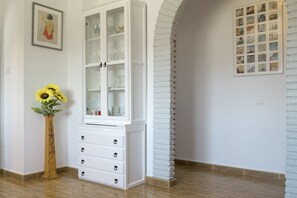 Ein weißes Schränkchen mit Glastüren, eine Holzzvase mit Sonnenblumen und ein gerahmtes Bild an der Wand.