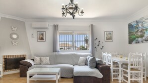 A living room with a sectional sofa, a dining table with chairs, a chandelier, and artwork on the walls.
