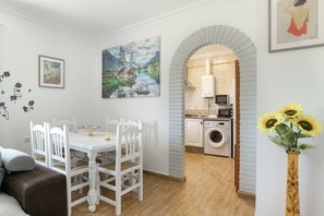 Ein Essbereich mit einem weißen Tisch und Stühlen, eine Küche inklusive Waschmaschine und ein gerahmtes Bild an der Wand.