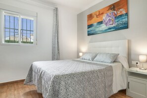 Ein Schlafzimmer mit Bett, Gemälde, Fenster und Nachttisch.
