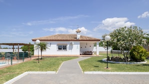 A white building with a tiled roof, a covered patio, and a paved walkway leading to the entrance.