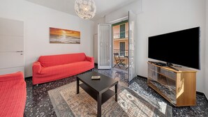 A living room with a red sofa, a coffee table, a TV on a wooden stand, and a patterned rug. - Apartment for 5 Guests Steps from the Sea (Moneglia)