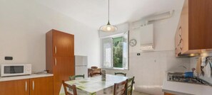 A compact kitchen with a dining table, wooden cabinets, a microwave, and a window providing natural light.