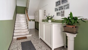 A staircase with a handrail, a white cabinet with a basket, a potted plant, and a wall with framed pictures. - Apartment for 5 Guests Steps from the Sea (Moneglia)