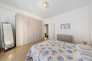 A bedroom with a bed, a wardrobe, a mirror, a bedside table, and a lamp.
