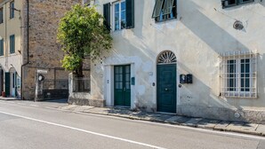 A street view with a building featuring a green door, a tree, and a stone wall.