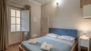 A bedroom with a bed, a nightstand, a lamp, a window with curtains, and a door.