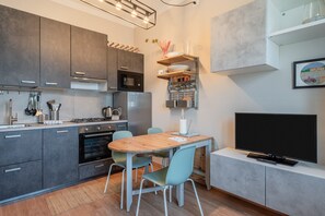 A modern kitchen with grey cabinets, a wooden dining table, and a flat-screen TV.