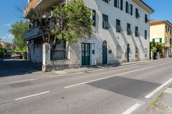 Un bâtiment à deux étages avec une porte et des fenêtres vertes, un arbre devant et une rue dégagée.