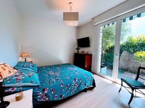 A bedroom with a bed, a desk, a chair, a TV, and a sliding glass door to the outside.