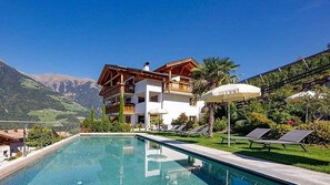 Un chalet de dos pisos con piscina, rodeado de montañas.