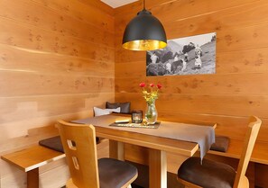 Un intérieur en bois comprenant une table à manger, des chaises, un luminaire suspendu noir, un vase avec des fleurs et une photographie en noir et blanc accrochée au mur.
