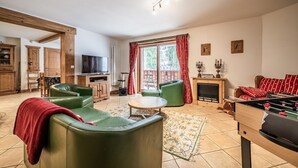 A living room with green sofas, a foosball table, a TV, and a fireplace.