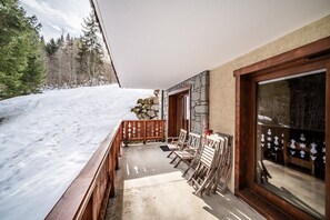 A wooden deck with chairs, a stone wall, and a glass door.