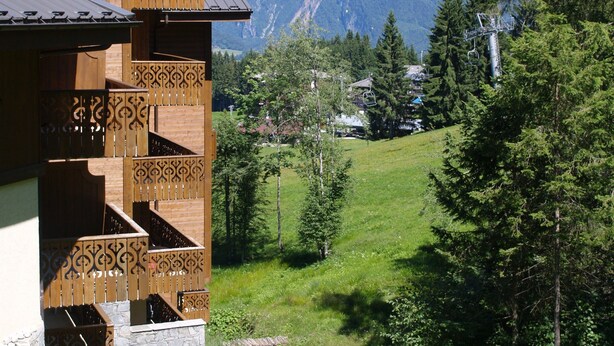 A chalet with a balcony, a mountain backdrop, and a grassy area.
