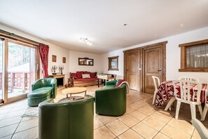 A living room with a sofa, green armchairs, a dining table with chairs, a fireplace, and a sliding glass door.