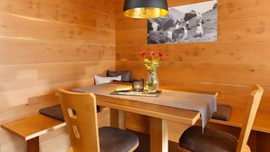 Un intérieur en bois comprenant une table à manger, des chaises, un luminaire suspendu noir, un vase avec des fleurs et une photographie en noir et blanc accrochée au mur.