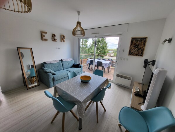 Ein modernes Wohnzimmer mit Sofa, Esstisch, Stühlen, einem großen Spiegel und Blick ins Freie.
