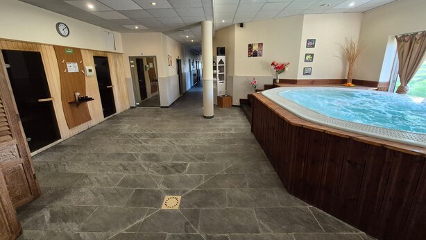 Ein Wellnessbereich mit Whirlpool, Steinböden, Holztüren und einer Uhr an der Wand.