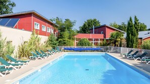 Ein Pool mit Liegestühlen, umgeben von roten Gebäuden und Grünpflanzen.