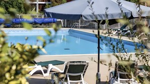 Ein Schwimmbecken mit Liegestühlen und Sonnenschirmen, umgeben von einer Hecke und Pflanzen.