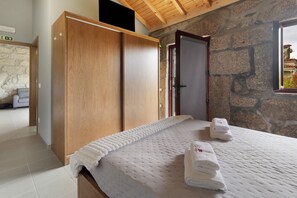 Une chambre avec un grand lit, une armoire en bois, un mur en pierre et une fenêtre donnant sur un beau paysage.