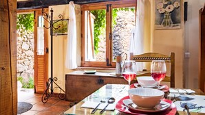 Un tavolo apparecchiato con piatti, ciotole e bicchieri da vino, una sedia di legno e una finestra che si affaccia sul verde.