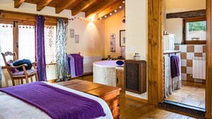 Una camera con un letto, travi in legno a soffitto, bagno con vasca e vista sull'esterno.