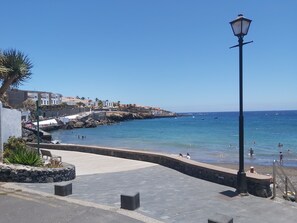A coastal promenade with a stone pathway, a lamp post, and a view of the sea and buildings.