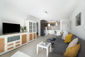 A modern living room with a flat-screen TV, a sofa, a coffee table, and a dining area in the background.