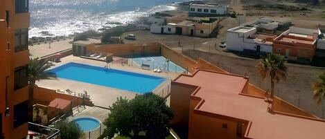 A residential area with a swimming pool, a beach, and a lighthouse in the distance.