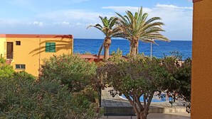 Ein Küstengebäude mit Blick auf das Meer, umgeben von viel Grün und einer Palme.